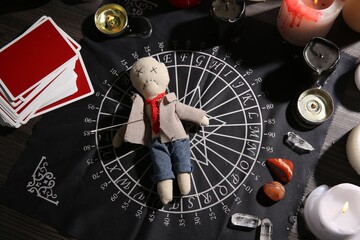 Voodoo doll pierced with needle surrounded by ceremonial items on table, flat lay. Curse ceremony