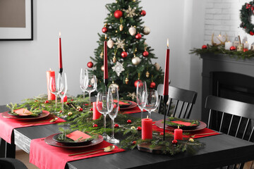 Elegant Christmas table setting with dishware and burning candles in festively decorated room