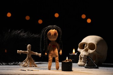 Female voodoo doll with pin in heart and ceremonial items on wooden table against blurred background