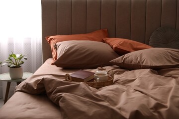 Cup of hot coffee and books on bed with stylish linens in room
