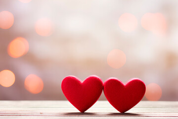 selective focus of two red hearts one next to the other placed on a wooden desk with blurred lights in the background, front view, Valentines theme, pink bokeh, horizontal, copy space