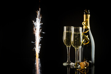 Champagne bottle and two glasses on a black background with sparklers. New Year and Christmas celebration concept.