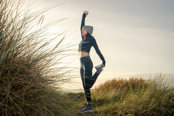 Sporty woman stretching her legs, doing standing quadricep front thigh stretch before running...