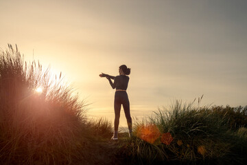 silhoutte of a sporty woman doing an arm stretch exercise at sunrise.