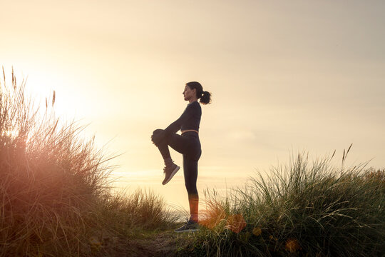 silhoutte of a sporty woman doing a leg stretch exercise at sunrise.