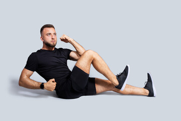 Obraz premium Serious strong young caucasian guy with beard in sportswear make exercises for abs, legs