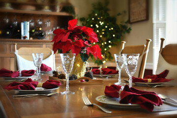 Dining room table set for a holiday meal with dishes, glasses, red napkins & centerpiece poinsettia