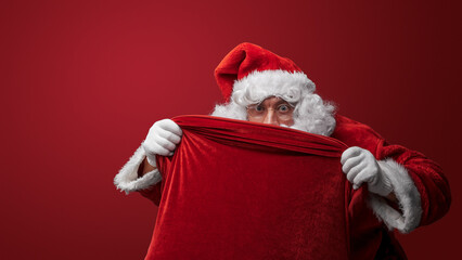 Santa Claus peeking over a red sack, eyes filled with Christmas excitement
