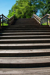 Obraz premium This is a photo of a wooden staircase in a park with a metal railing, surrounded by trees under a blue sky.