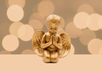 Golden angel figurine in front of a bokeh background. Copy space.