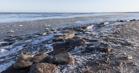 Melting ice floes lay on frozen coast of Baltic Sea on a daytime