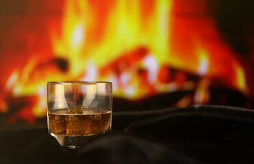 Whisky or whiskey or bourbon with ice on wooden surface on fireplace background. Luxury elite alcohol in wide glass. Low key dark scene