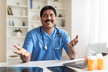 Medical Consultation. Indian Male Doctor Sitting At Desk And Talking At Camera