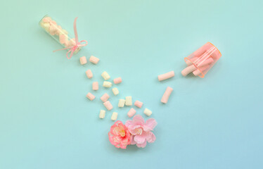 Metaphorical concept of care for flowers. Pink flower sprayed with marshmallows from small transparent tanks on a pastel blue background. Minimal flat lay composition. Top view