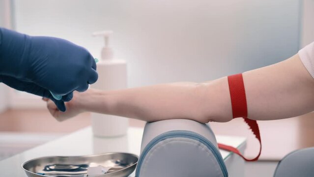 Laboratory worker doctor takes a blood sample for analysis. A young woman donates blood from a vein for analysis in a clinic. Close up of hand.