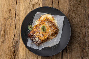 Bolognese lasagna in a black plate on a wooden table. Close up