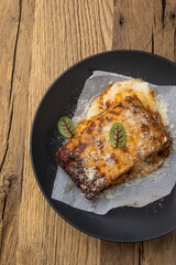 Bolognese lasagna in a black plate on a wooden table. Close up