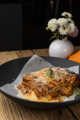 Bolognese lasagna in a black plate on a wooden table. Close up