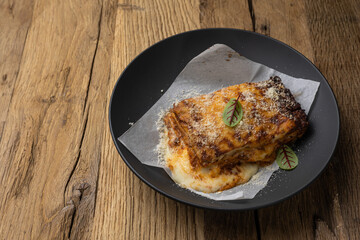 Bolognese lasagna in a black plate on a wooden table. Close up