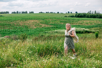Naklejka na ściany i meble Beautiful woman walking in a summer field with a jacket over her shoulder