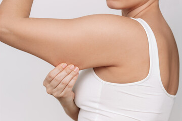 Cropped shot of a young woman grabbing skin on her upper arm with excess fat isolated on a white...