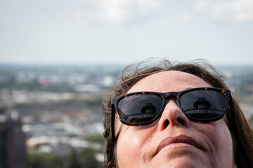 female tourist in Rotterdam look up at the Euromast tower which is seen in the reflection of her sunglasses. Dutch cosmopolitan city in background, clear day in the Netherlands for sightseeing