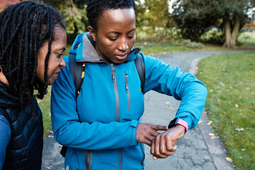 Two mature black women checking smart watch in a park.