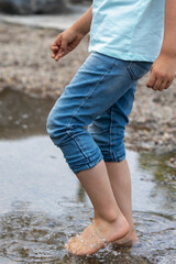 Close-up of bare feet of boy in blue clothes. A child splashes in a puddle on a warm summer day