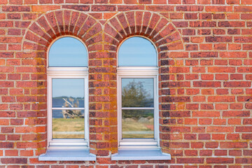 Fototapeta na wymiar Ancient red brick wall, daylight, with two arched windows. Horizontal photo