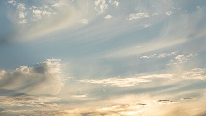 Obraz premium The summer evening sky with cirrus clouds is slightly illuminated by the yellowish sunlight.