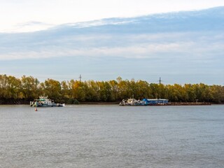 A pusher tug tows a dredger along the Kuban River on an autumn day on the day navigation is closed - obrazy, fototapety, plakaty