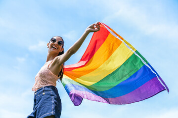 Exuberant young lady waves a vibrant LGBTQ+ flag in the air, embodying the spirit of Pride.