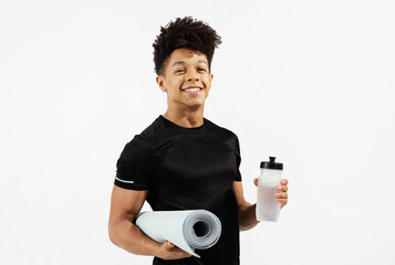 Athletic man holds water bottle and fitness mat, white backdrop
