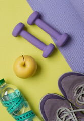 The concept of a healthy lifestyle, fitness, proper nutrition. Sneakers, dumbbells, water and fruits on a bright yellow background.