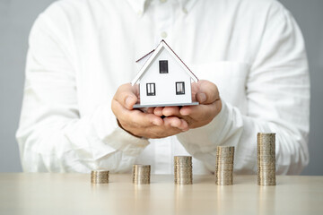Businessman  hand hold a home model on the stacked coin with many increase value on the desk in the office, Financial of real estate business investment and buy house concept.