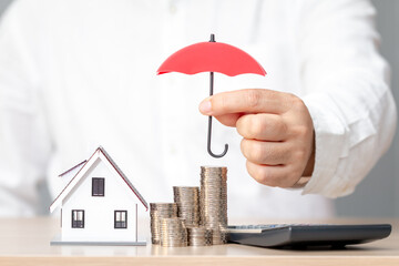 Businessman hand hold open the red umbrella for protect to home model and stack gold coin in the...
