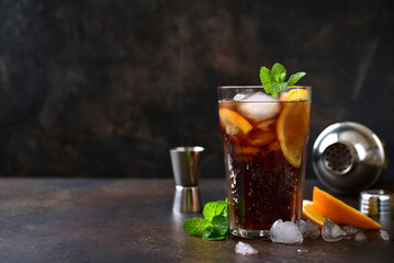 Cold summer soda cocktail with cola, dark rum and orange in a tall glass.