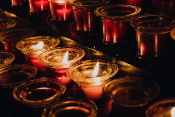 Candles in a dark Catholic Cathedral. Prayer, incense and Christian Faith. Row of small lit votive candles in red glass candlesticks on a candle holder stand in church. Religious tradition
