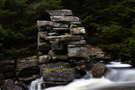 Stone foundation of old mill with long exposure stream of water in dark spruce forest in Scandinavia
