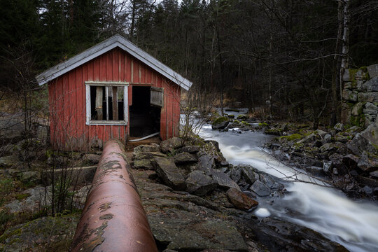 Stone foundation and house of old mill with long exposure stream of water in dark forest in Scandinavia
