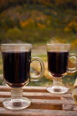 Two glass with mulled red wine on autumn forest background. Picnic with alcohol drinks. Vacations for two. Hot wine at the back yard. Aromatic gluhwein. Autumn travel. 