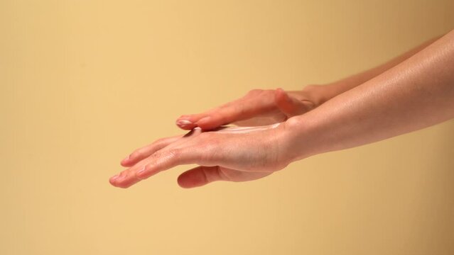 Female hands apply cream with finger and rub it on skin on beige isolated background. The concept of beauty and aesthetics, moisturizing and nourishing the skin