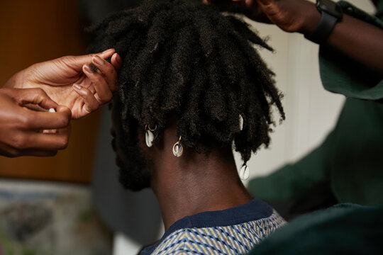 Close up friends decorating young black man's locs with shells and jewels