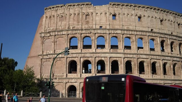 Bus past exterior facade of the Roman Colosseum from across street viewpoint on sunny morning. One of most famous destination in Italy. Concept of holidays, vacations and travel in Europe, slow motion