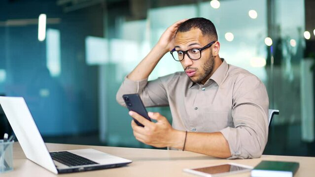 Shocked employee entrepreneur man looks at cellphone read unbelievable astonish news excited guy male wonder with mobile phone receive smartphone sms amazed say wow shock amazement at business office