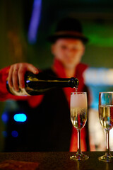 A bartender in a red shirt pours champagne into glasses at night