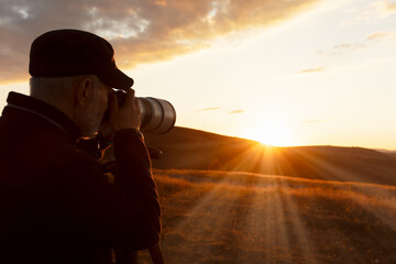 An adult man takes pictures of a picturesque sunset in the mountains with a long lens fixed on a...