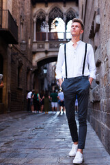 Fototapeta na wymiar Young European guy in shirt and trousers with suspenders walking around city