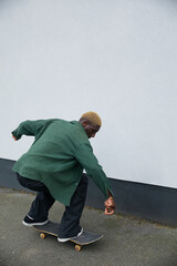 Fashionable black boy with blonde hair riding skateboard on sidewalk © Ejatu Shaw