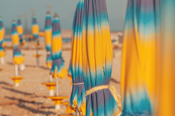 Folded colorful beach umbrella parasols on Adriatic sea coast in sunny summer morning, holiday and vacation background with copy space - obrazy, fototapety, plakaty